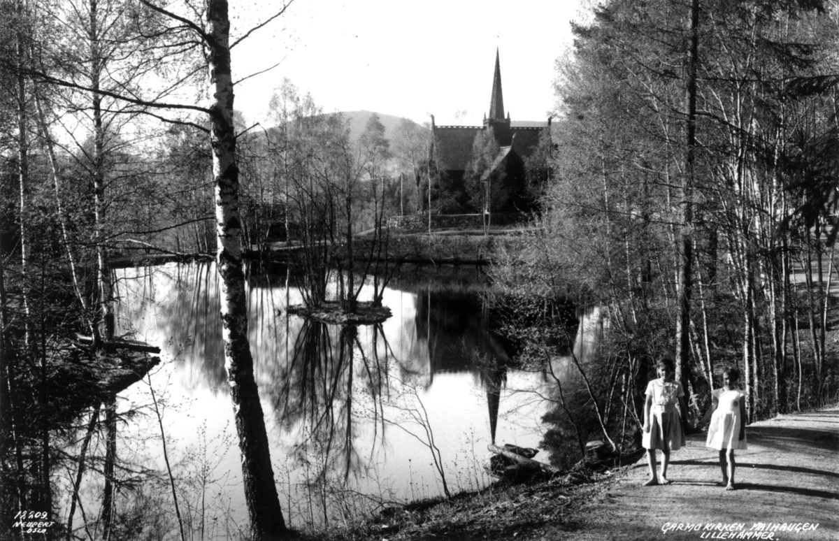 De Sandvigske Samlinger, Lillehammer 1935. Garmo kirke, Maihaugen. Vann omgitt av bjørketrær og veier.  I forgrunnen to småjenter på veien. 