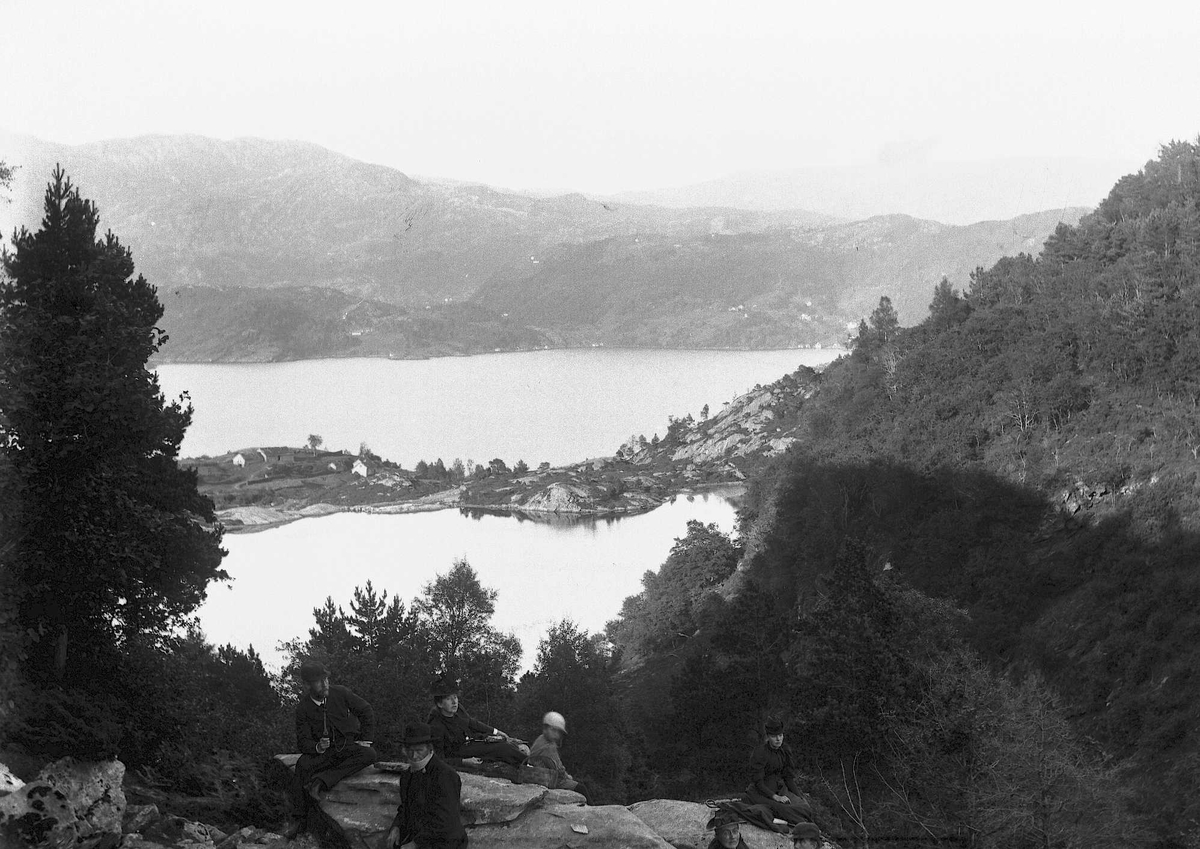 Fotografiet er tatt fra den gamle ferdselsvegen mellom Lifjorden og Hyllestadfjorden i Ytre Sogn. En gruppe voksne og barn tar en rast i forgrunnen.