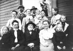 Familieportrett, stor gruppe mennesker foran bygning.
Famil