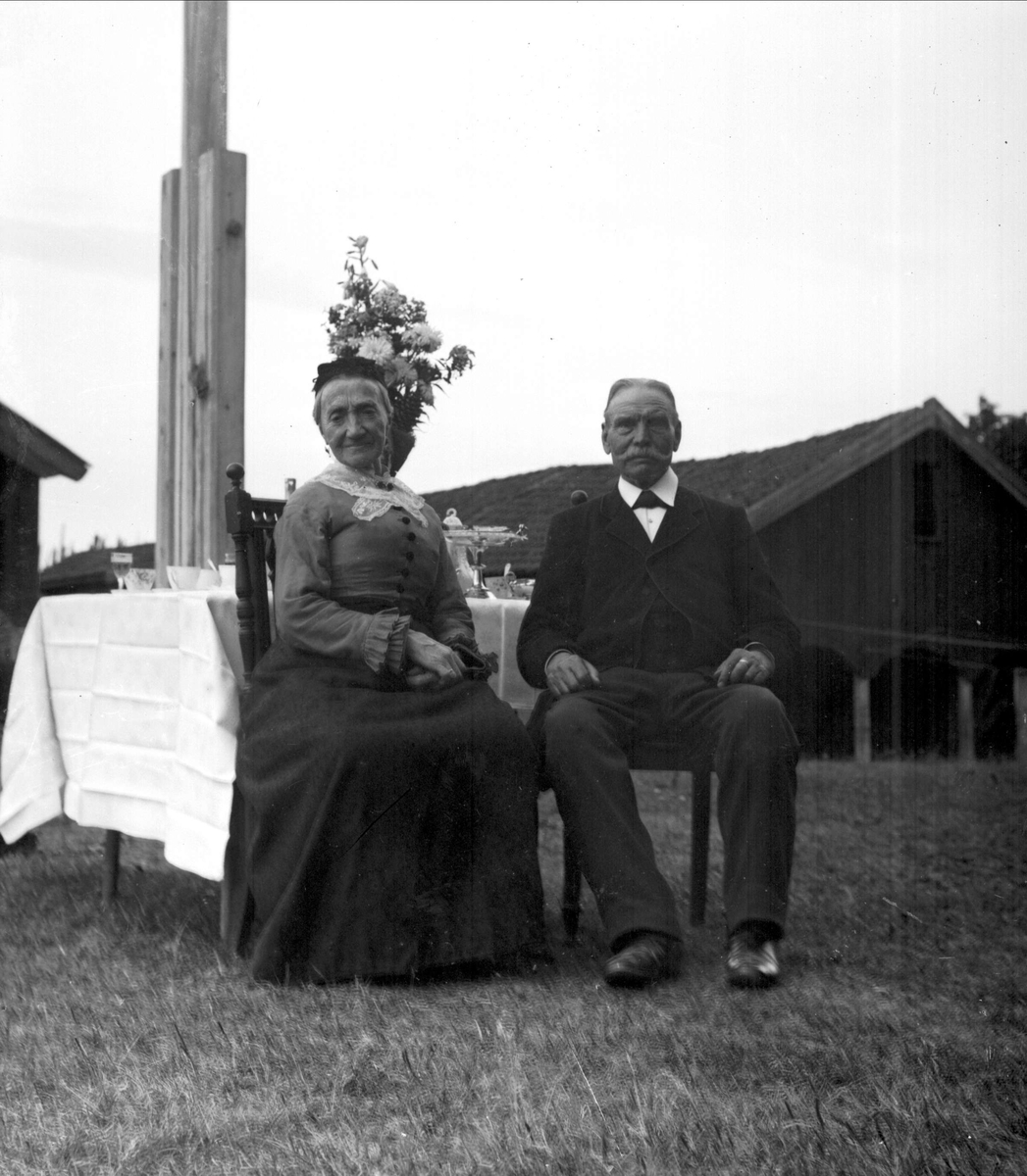 Gruppeportrett, mann og kvinne ved bord i hagen. Vinhandler Larsen sted på Bygdøy.