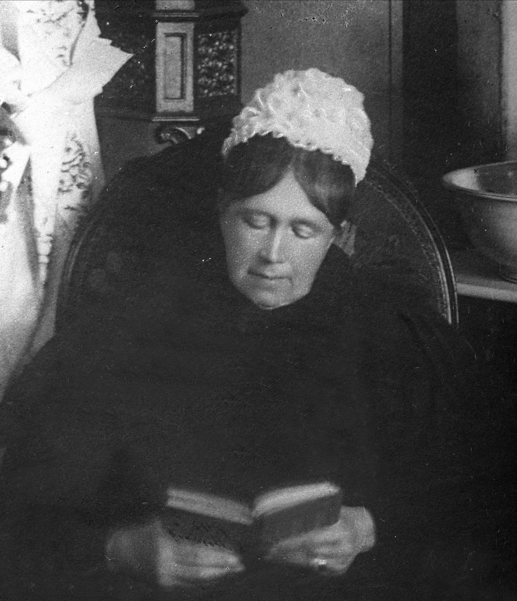 Portrett, eldre kvinne sitter og leser i en bok.