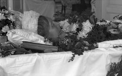 Post mortem-fotografi. Kvinne i pyntet kiste, bok ved hodet