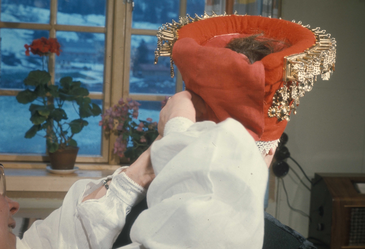 Brudepynting, Jølster 1967.Bruden, Eva Eide, får hjelp av Maria Gjesdal  med påkledningen.
Et rødt tøystykke festes over båndene i nakken. På den måten skjules båndene både på valken og sølvet.