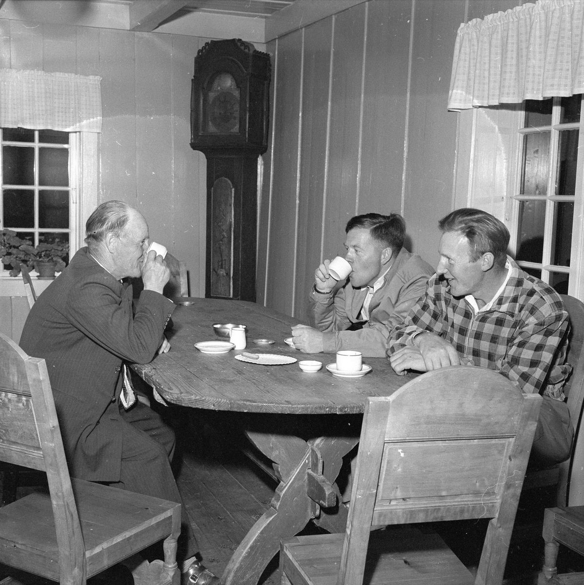 Finnskogen, august 1956. Marken. Interiør, tre menn drikker kaffe rundt bord.