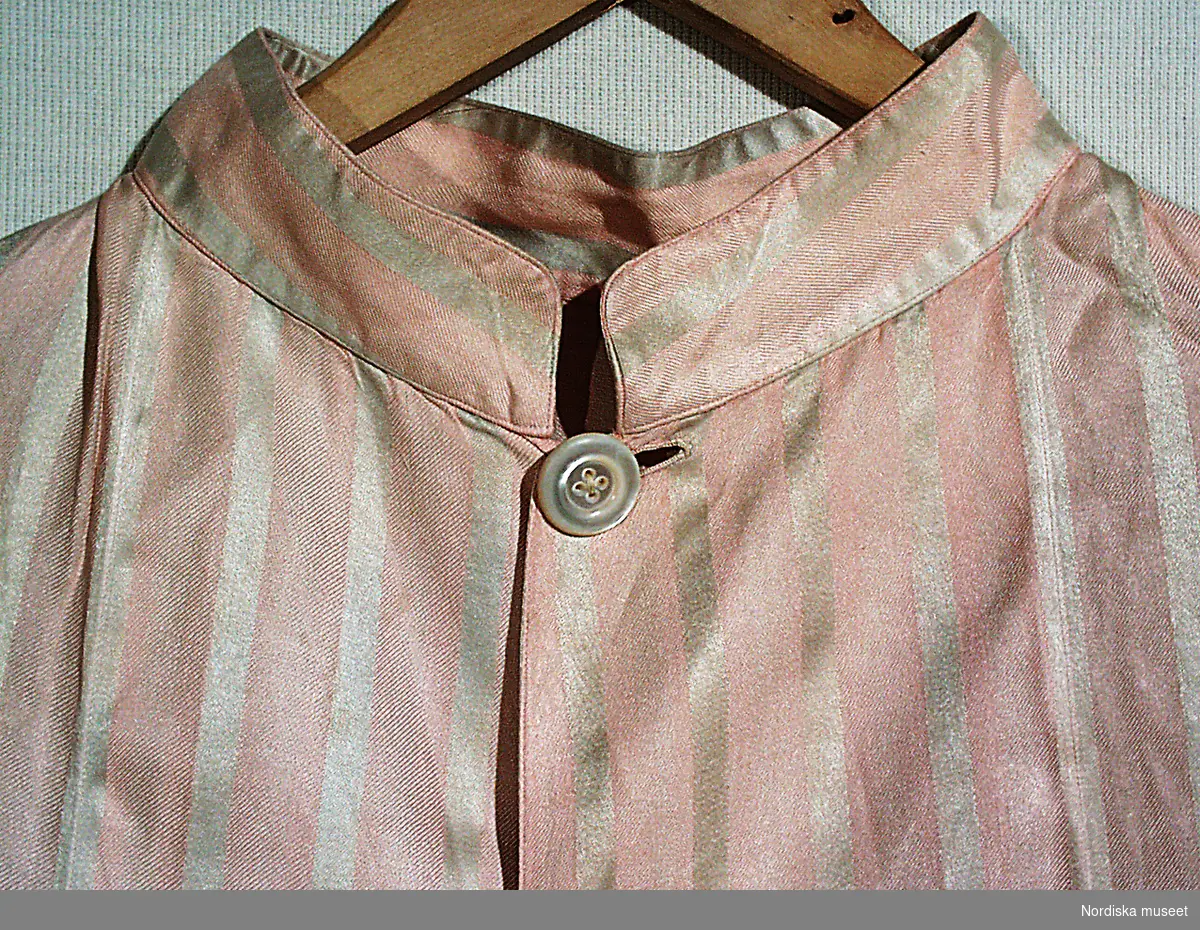 Pyjamas, rock (a) och byxor (b), av siden, rosa och grå ränder. Snodd m. 2 tofsar. Knappar av pärlemor.