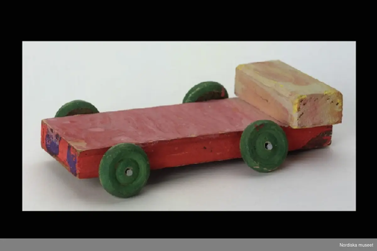Inventering Sesam 1996-1999:
L 16  B 7  H 4
Bil tillverkad av rödmålad lamellskiva med grönfärgade trähjul och gul förarhytt.
Jan Conradson (f. 1968) tillverkade bilen 1973 på  Kyrkans småbarnsskola i Djursholm. 
Birgitta Martinius 1996