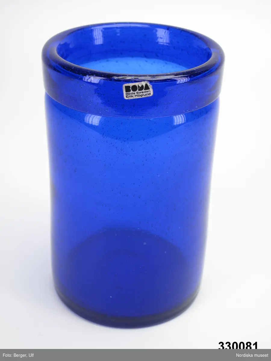 Vas, cylinderformad koboltblå glasvas med bred övervikt kant, slipat puntelmärke i botten. Blåsor i glasmassan. Klisteretikett på kanten. 
/Cecilia Wallquist 2010-03-01