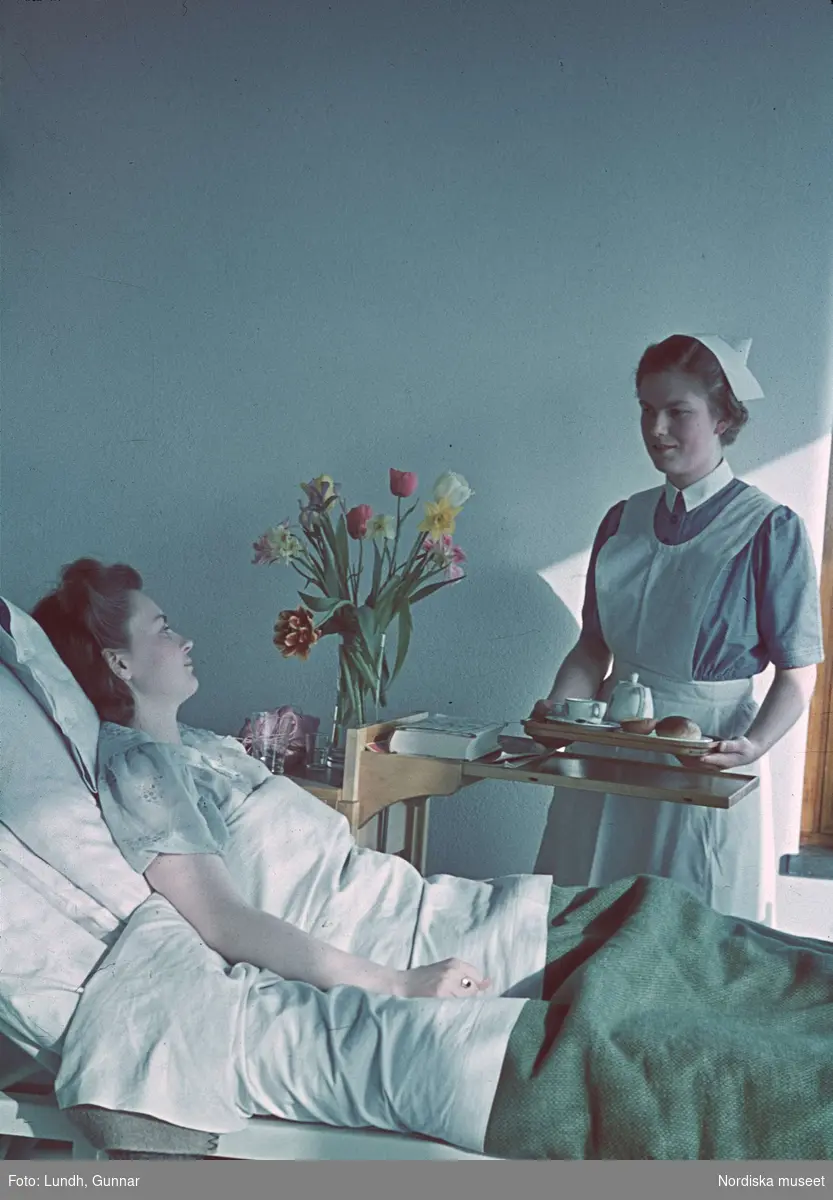 Kvinna i sjukhussäng. Sjuksyster med kaffebricka. 
