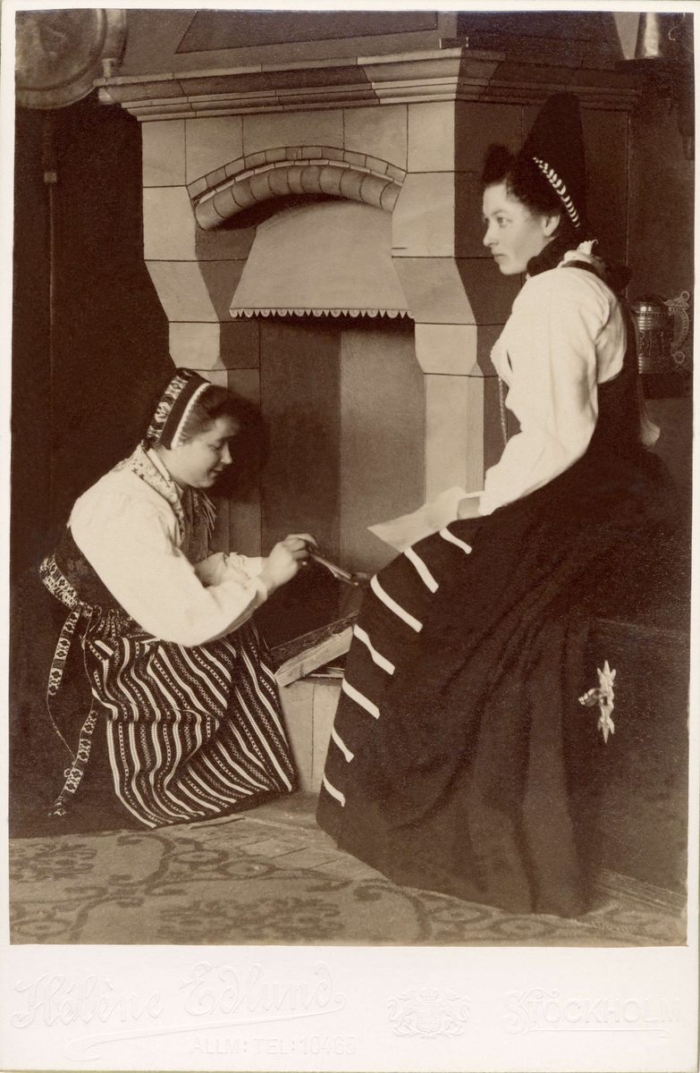 Två kvinnor sitter i ett kök, poserar i olika folkdräkter