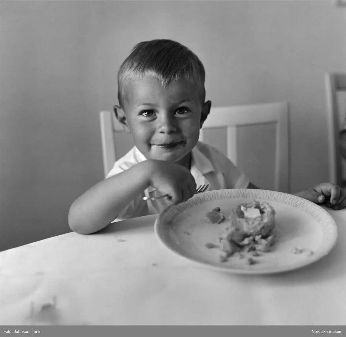 Liten pojke sitter vid matbord med gaffel i handen och mattallrik framför sig. "Pitepalt i Öjebyn".