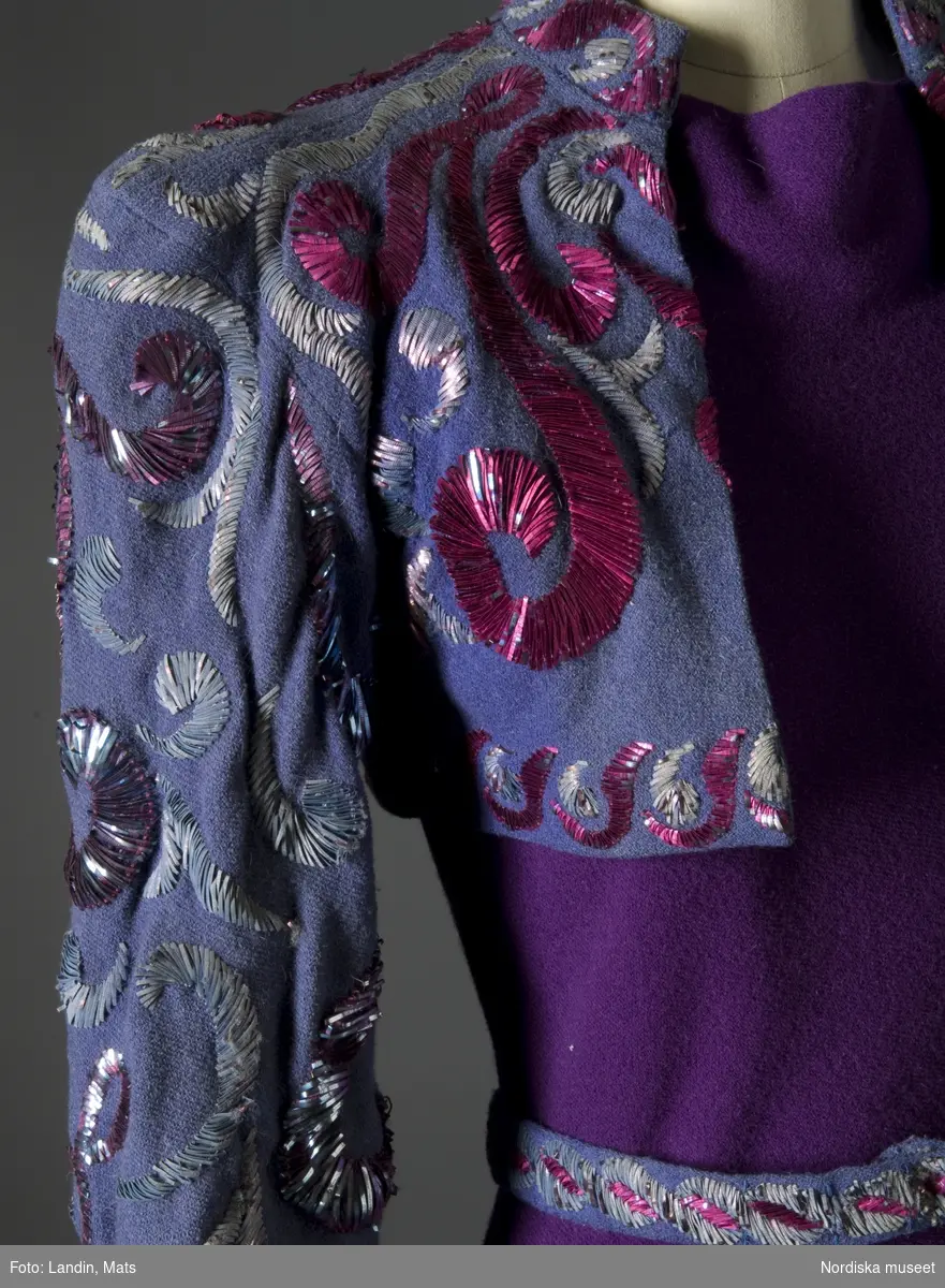 Aftonklänning av rödlila yllejersey med jacka i gråblått, rikt broderad i färger med metall-lan. Madeleine Vionnet, Paris 1938. Nordiska museet inv nr 236461.