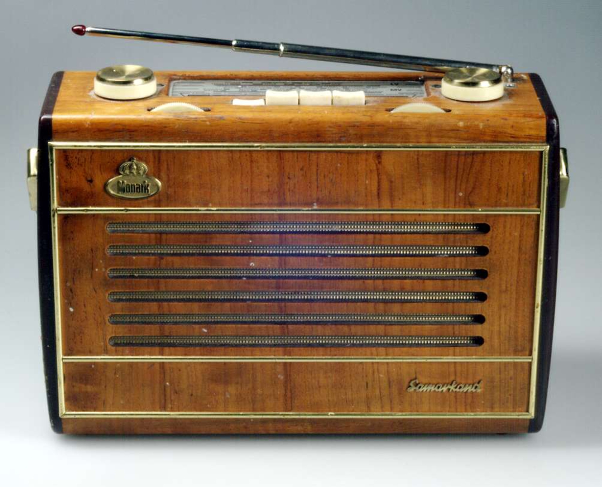 Transistorradio av fabrikatet Monark, modell Samarkand. Hölje av blindträ med faner. I sidorna målad med en vinröd/brun färg. Tar in UKV, KV, MV och LV.
