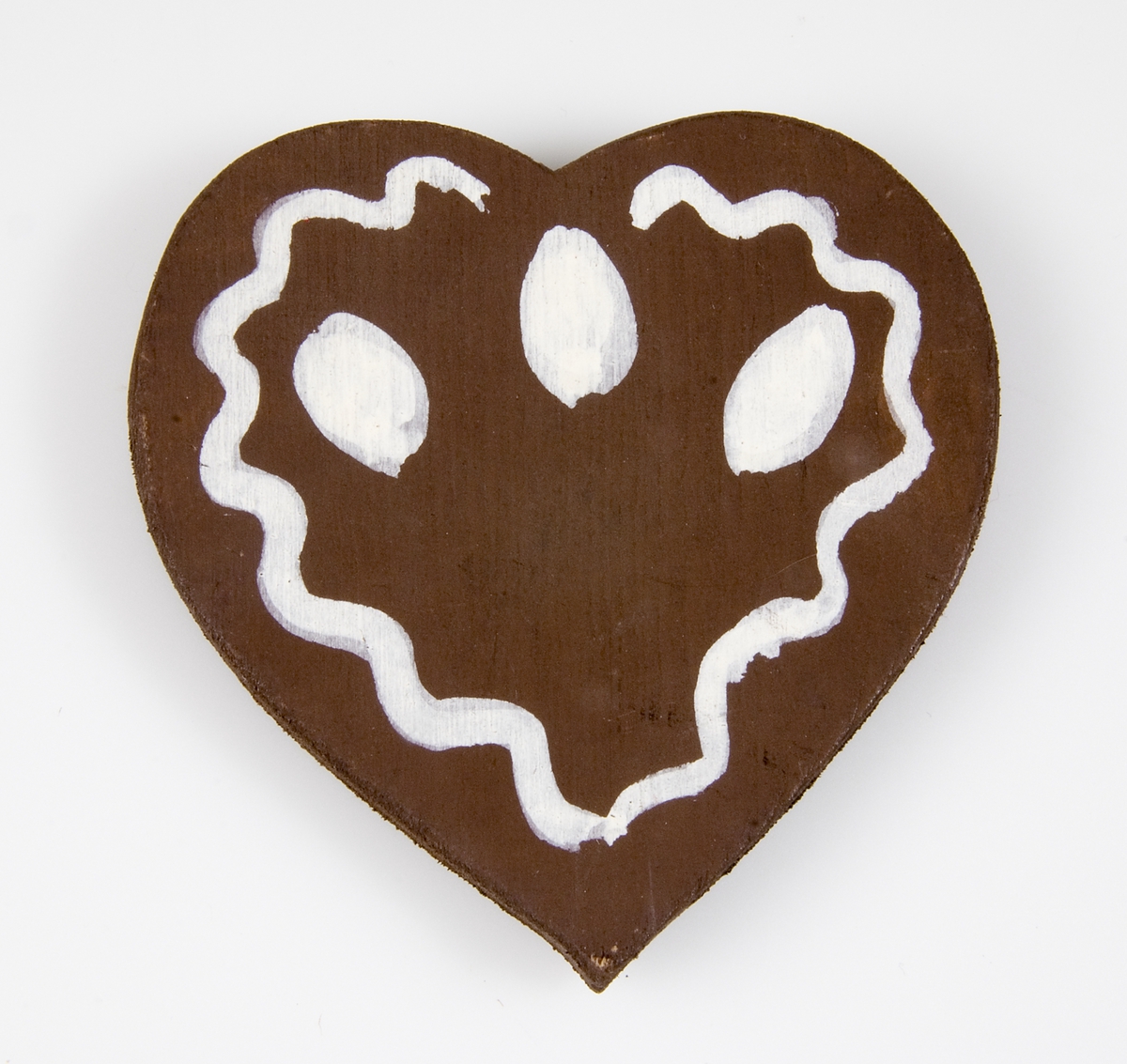 Julgransprydnad i form av ett pepparkakshjärta av brunmålat trä med vitmålade detaljer.
