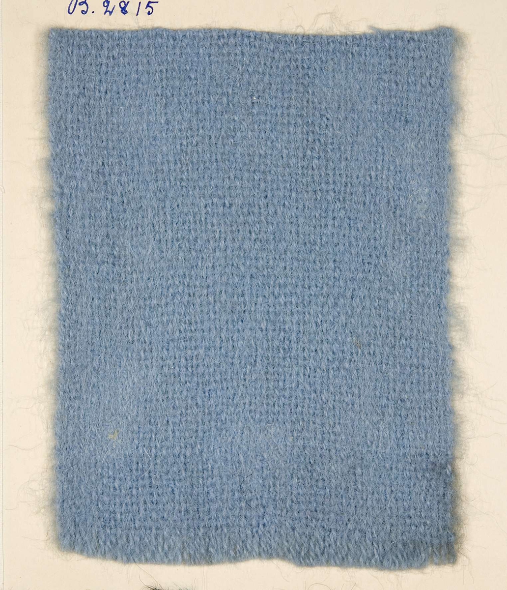 Vävprov ämnat för barnhalsduk vävt med ullgarn i tuskaft, ljusblått. Vävprovet har nummer "B-2815".