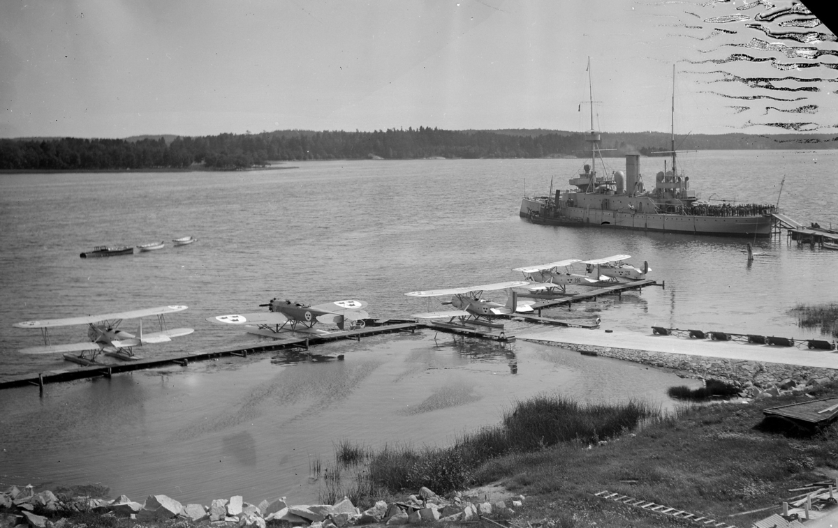 Slipen på F 2 Roslagens flygflottilj, 1929. Flygplan S 5 och SK 4 förankrade vid brygga och fartyget H.M.S Göta förankrat bredvid. På fartygsdäcket står en folksamling.