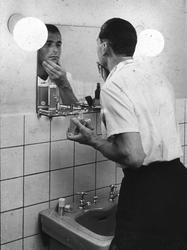 Mann tar på etterbarberingsvann foran speilet, 1930-tallet