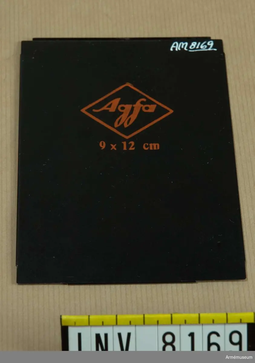 Samhörande nr är AM 8151 - 8199.
En romb ringar in ordet Agfa och under romben står 9 x 12 cm - allt står med orange text på svart bakgrund.Inlägget placeras i en kassett avsedd för plåtar vid fotografering på bladfilm. Ur fotomaterielsats 7 för Brückner resekamera.