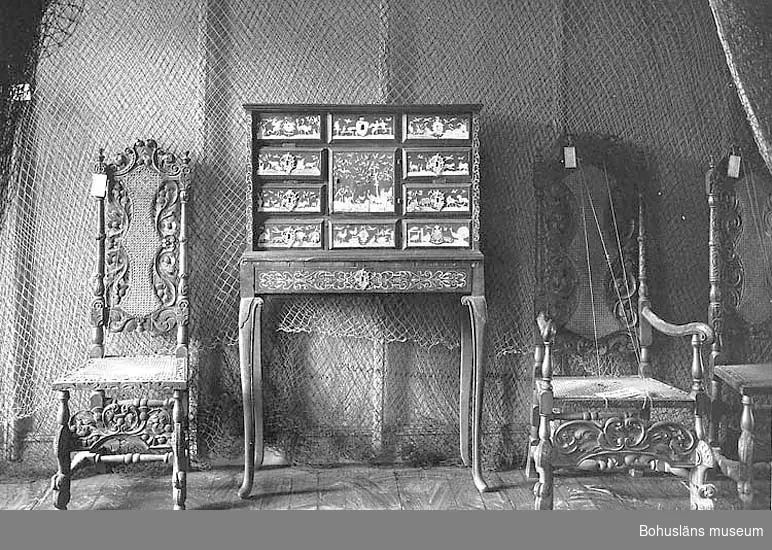 Föremålet visas i basutställningen Uddevalla genom tiderna, Bohusläns museum, Uddevalla.

Kabinettskåp från 1600-talet med dekor av metallintarsia, senare fotställning. Enligt äldre katalogupgifter ett krigsrov från 30-åriga kriget.
Skåpet har sju lådor och ett mittfack med dörr. Den översta lådan är utformad som tre lådförstycken och den nedre högra lådan är utformade som två lådförstycken.
Lådförstyckena, mittdörren och sidornas framkant har en intarsia av trä och metall. Runt lådförstyckena och mittdörren en profilerad list. Metallintarsians figurer föreställer träd, buskar, och olika djur från Afrika, Asien och Europa samt ur mytologins värld. Metallintarsian har gravyrer. Åtskilligt av tenndekoren har fallit bort och ersatts med tennliknande färg. Innanför luckan två lådor. Insidan luckan och på lådornas lådförstycken träfaner i rutmönster. Framkant på skåpsidorna har träfaner och metallintarsia i bladslingor, akantusslingor. Sidornas och ovansidans faner i valnöt är lagt i trekanter vilka bildar kvadrater, ett rutmönster. 
Skåpets blindträ är fur eller gran, i två av lådförstyckena blindträ av lövträ. Lådsidor och lådbottnar av ek. Träfanér och listverk är troligen tillverkade i träslaget palisander (jakaranda). Metallintarsian är i tenn med en tillsats av koppar. Lådförsstyckena är uppbyggda i tre lager, innerst furu, sedan ytterligare ett lager i gran eller fur och ytterst ett faner. Luckans gångjärn är av mässing.
Fotställningen med ben i senbarock, senare tillagda, ca 1725 - 1750. Fällbar lucka och innanför denna ett inrikte med tre lådor.
Luckans och lådornas metallintarsia är utformade som stiliserade bladslingor och blommor. Fotställningen sidor är fanerade med stående faner, troligen palisander. Luckan har tennintarsia med tillsats av koppar och bly. Ben av furu som är betsade i rödbrunt. Blindträ i lådförstycken, sidor och bottnar är i ek.
I samband med konservering av möbeln konstaterades fläckar av bläck i flera av möbelns lådor.
Enligt äldre fotografi i BM:s bildarkiv nr 948 i arkivbox "Bilder rörande museets samlingar", har det funnits sex nyckelskyltar i rokoko, samtliga borta. 

I gammalt urklipp, se Bilagepärmen UM2551 framgår att möbeln skänktes till museet åtföljd av följande skrivelse:
"Till Bohusläns Museum! Undertecknad, bohuslänning, som köpt medföljande möbel i närheten av Kongelf, och om hvilken det säges att den skall vara eröfrad ifrån en tysk prins under 30-åriga kriget, tror derför att den som trofé bör erhålla sin blifande plats å Bohusläns Museum, och hvarom anhåller ödmjukligen. Göteborg den 30 Aug. 1862. J. BERGMAN gen J. Bergman.

Ur handskrivna katalogen 1957-1958:
Chiffonier i barock KABINETTSKÅP
a) Överdelen: L. 91; Br. 33; H. 58,5 cm; 1 skåp och 7 draglådor; valnötsfaner, m. inläggningar av tenn? b) vars framsida har inläggn. som a). Hela möbeln mkt illa åtgången, de flesta inläggningarna ha fallit av och hålen målats i m. silverbrons. Nycklar saknas.

Lappkatalog: 82
Skåp
Kabinettskåp med fotställning

Litteratur:
Wallin, Sigurd: Nordiska museets möbler från svenska herremanshem. Del I, 1500-1600-talen. Renässans och barock. Nordiska museet 1931 - 1935. Facsimile-upplaga 1979.
Francén, Richard: Konservering av ett kabinettskåp. Stiftelsen Västsvensk Konserveringsateljé. Årsskrift 1992.