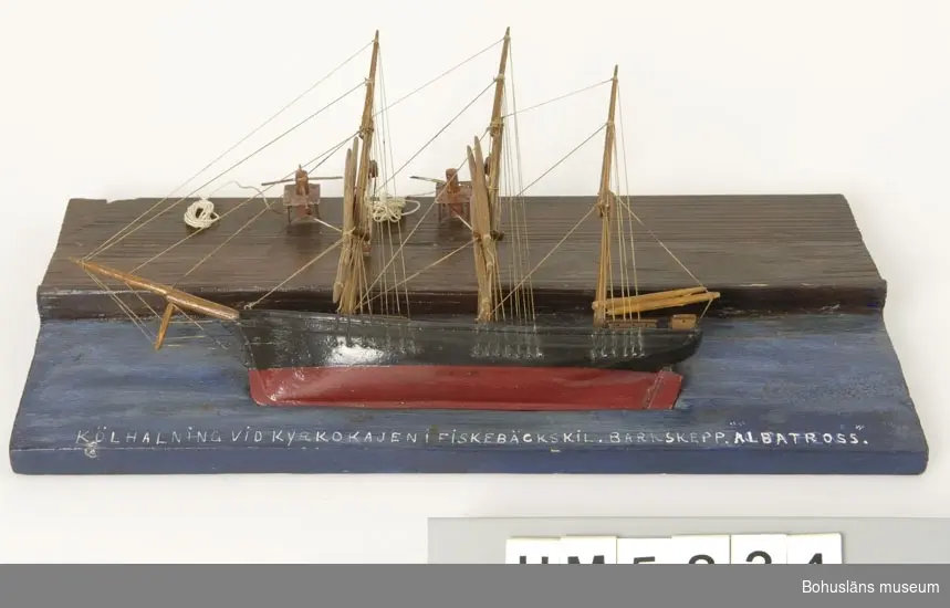 Modell av kölhalning av tremastade barken Albatross på Kyrkokajen, Fiskebäckskil. Tillverkad av kapten John Emil Olsson (1880-1950), Fiskebäckskil på Skaftö i Lysekils kommun på 1940-talet.
Trä, metall, lintråd, målat med oljefärg.
Fartygsmodell längd 30 cm, bredd 4 cm, höjd 20 cm. Platta: 40 x 19 cm; okänd skala. Blockmodell målad i  svart och rött. Stående och löpande rigg. Däckshus och lastluckor.
Monterad på en rektangulär platta med blåmålad vattenyta och brunmålad träkaj. Modellen ligger långsides med riggen nedhalad mot kajen. Två vinschspel på kajen fästade i fock- och stormast med två treskivade block i varje. Fällda rår. På modellens ovansida står textat med vita tryckbokstäver: 
KÖLHALNING VID KYRKOKAJEN I FISKEBÄCKSKIL. BARKSKEPP. "ALBATROSS".
Kölhalning innebär att skeppet krängs på sidan så att skrov, botten och köl kan repareras och underhållas.

Definitioner:
Bark - segelfartyg med tre eller fler master med rår på alla master och ett gaffelsegel på den aktra.
Råsegel - rektangulärt eller trapetsformigt segel som förs på en rå, dvs. en horisontell stång fäst vid mastens framkant
Gaffelsegel - trapetsformat segel fäst längs akterkanten av masten och med sina övre (kortare) och undre (längre) lik (kanter) fäst vid två rundhult (gaffel resp. bom).

Kyrkokajen eller Kyrkekajen, Fiskebäckskil:
Under segelsjöfartens storhetstid på 1860- och 70-talen fylldes Kilen på vintern av fartyg som låg uppankrade hemmavid. Det var på vintern man hade möjlighet att se över och underhålla fartygen inför nästa seglationsperiod.  Epoken varade fram till 1930-talet då segelskutornas tid var förbi. 
Vid Kyrkekajen ligger idag Skaftös skolsegelfartyg T/S Kvartsita.

Ur handskrivna katalogen 1957-1958:
Kölhalning av "Albatross"
Modell på platta. Kölens mått 19,5 Föremålet helt.
Från kapten Olssons saml., Fiskebäckskil.

För ytterligare information om John Emil Olsson och förvärvet, se UM005807.

Föremålet presenterat på Bohusläns museums hemsida år 2009 - 2013, webbutställning "John Emil Olsson Fiskebäckskils sjöfartsmuseum".