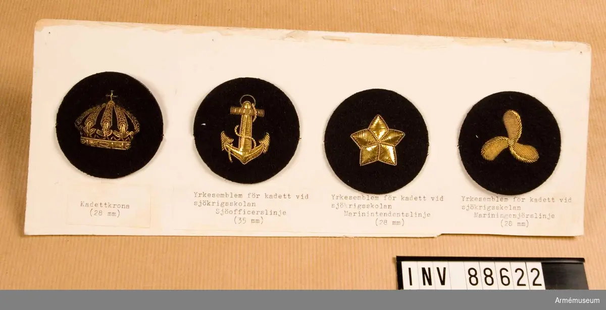Fyra tygmärken: kadettkrona, kadett vid sjöofficerslinjen, kadett vid marin-intendentslinjen, kadett vid mariningenjörslinjen.