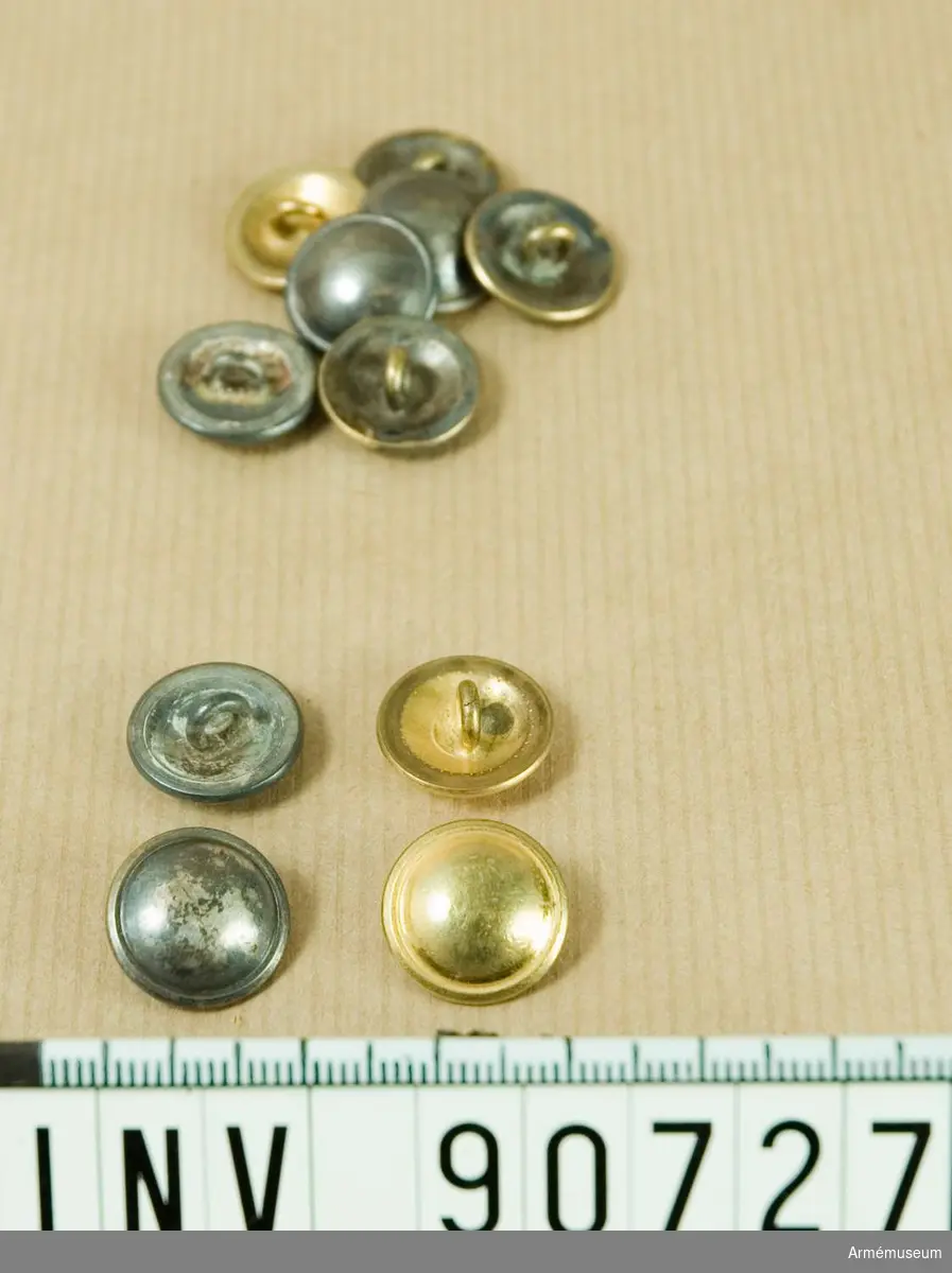 Låda innehållande åtta silverfärgade och tre guldfärgade små knappar till kolett.