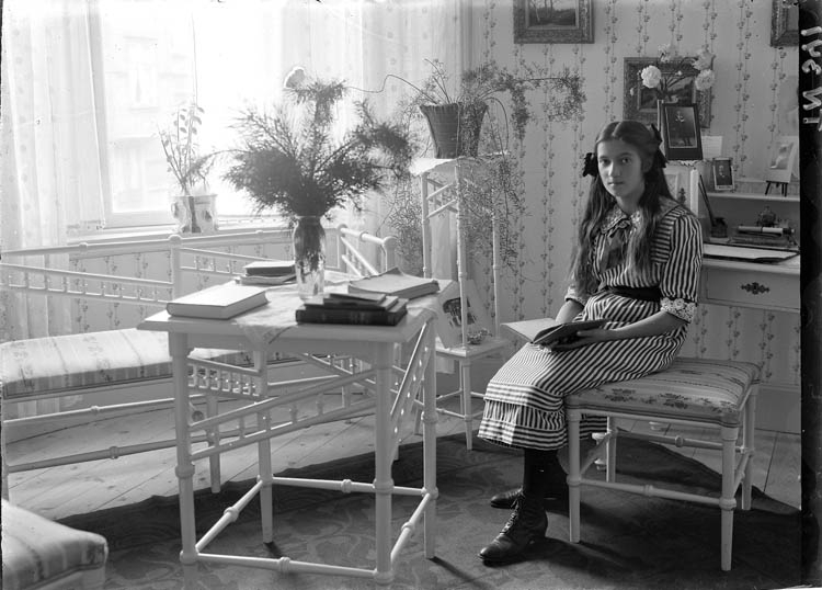 "Ung flicka i privat hem". Flickan på bilden är fru Maja Källner, född Radyn, möblerna finns 1977 i villa Majsol på Gustafsberg." enligt notering.