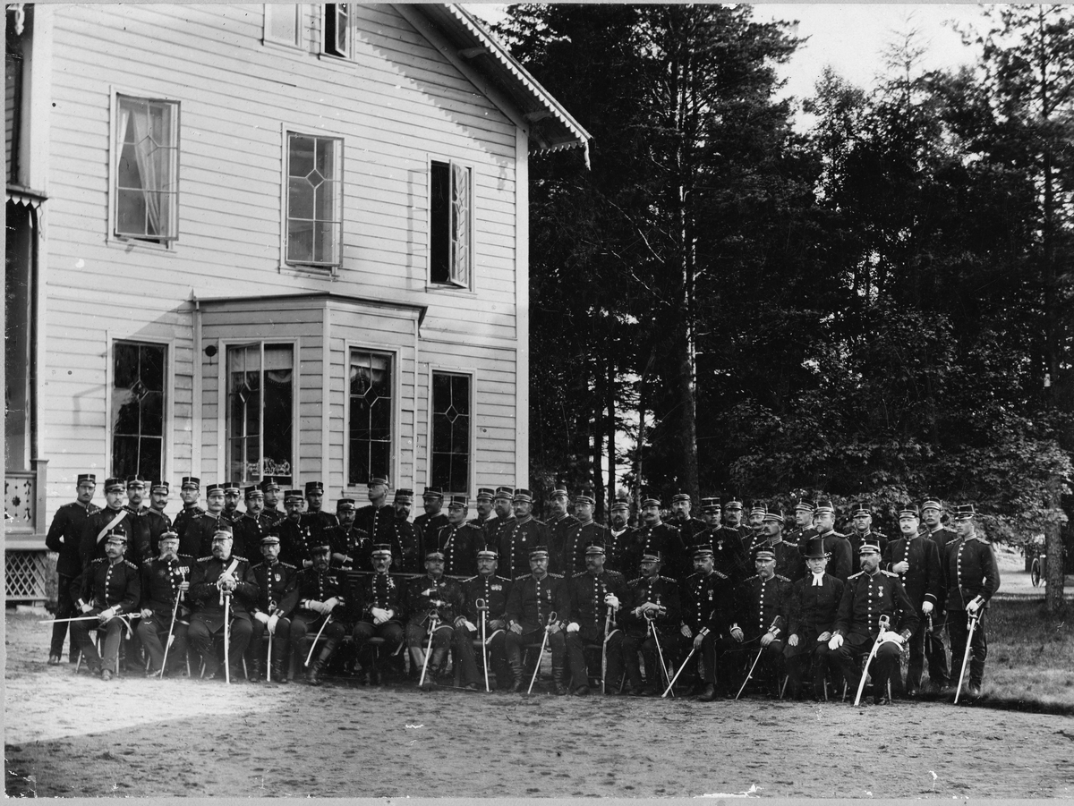 Officerare vid Älvsborgs regemente I 15 samlade till grupporträtt utanför byggnad på Fristad hed, I främre raden näst längst till höger sitter en präst.