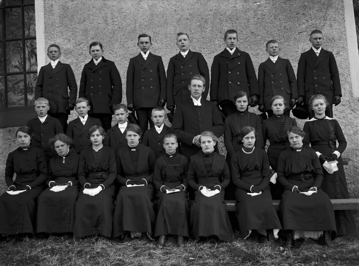 Konfirmandgrupp, sannolikt vid Veckholms kyrka, Uppland, troligen 18 april 1914. I mitten komminister Mats Åmark (1882-1973).