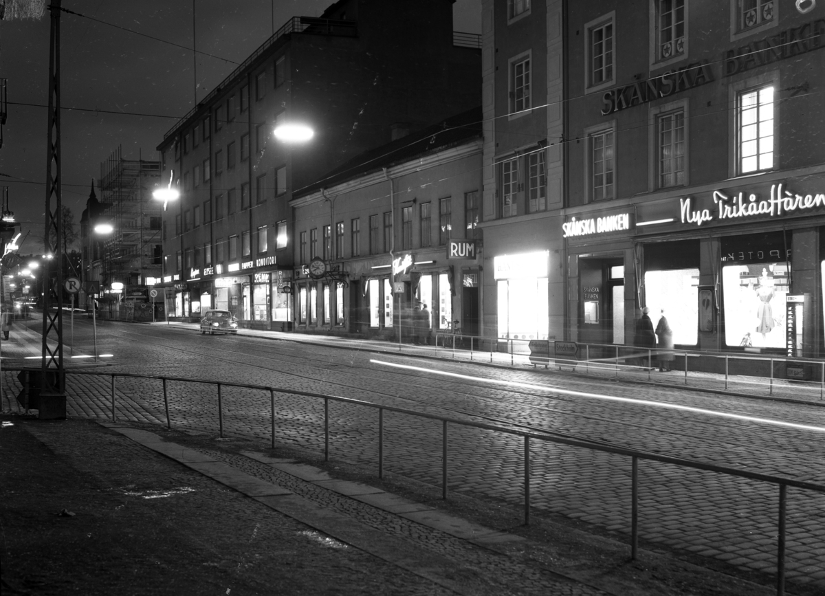 Neonskyltarna lyser upp Västra Storgatan i Jönköping den 9 april 1958.Till vänster Västerhuset och i mitten Västra Storgatan 4 med Engströms Ur och Konstflit. Till vänster om Skånska banken ligger en nyöppnad butik med namnet Handskcentrum. Till höger om Skånska bankens ingång ligger Nya Trikåaffären som hade en automat på fasaden för den som behövde köpa strumpor när butiken var stängd.
