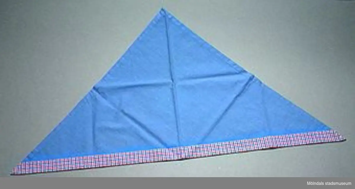 En skolkökssnibb i blått och rosablåvit-rutigt tyg. Undervisningsmaterial för årskurs 6. Samhör med 02663-02669. Övriga uppgifter se 02643:1.