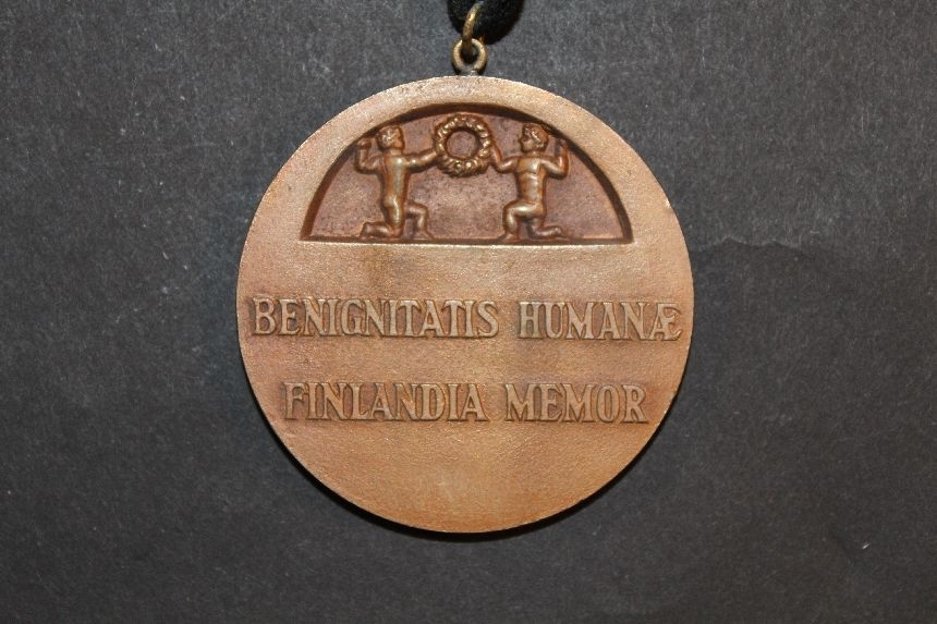 Medalj i brons, rund, kallad Benignitatis humanae Finlandia memor. Denna text återfinns också på frånsidan under ett par unga pojkar som håller i en krans. Frånsidan visar i relief en kvinnofigur, en olivkvist samt en brinnande oljelampa. Upptill, på medaljens rand, sitter en ögla genom vilken det löper ett svartsammetsband, ca 700 mm långt. Medaljen tilldelades överpostexpeditör (öpx) Brita Helena Kihlberg (född Östman) i december 1946 "såsombevis på erkänsla för uppoffrande arbete för de nödlidande i Finlandåren 1941 - 46". Den medföljande handlingen till medaljen
(se dokumentsamlingen II135a) är undertecknad av Finlands president Paasakivi och landets socialminister. Fru Kihlberg levde mellan1901-10-13 : 1955-11-20.