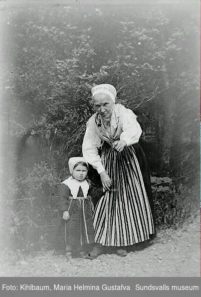 Porträtt. Kvinna med barn klädd i folkdräkter i utemiljö.