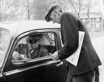 Postkunden Anton Olofsson i Rumpeboda får dagens post av bilkåkande lantbrevbäraren Cyril Falk på linjen Lönsboda-Hunshult-Björkhult-Lönsboda.  
Foto maj 1961.