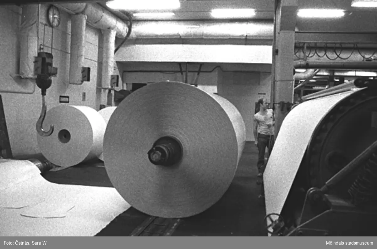 Pappersbalar i Byggnad 6, KM 2 till höger. Jan Callesen ses i bakgrunden.
Bilden ingår i serie från produktion och interiör på pappersindustrin Papyrus, 1980-tal.