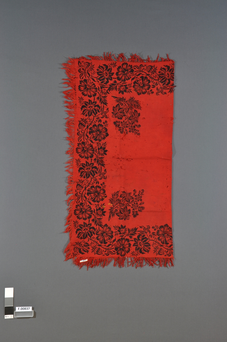 Rødt sjal med svart trykket blomsterdekor og frynser. Kvadratisk.