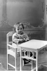 Studioportrett av liten gutt som sitter ved et bord.