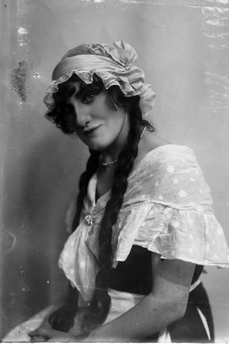 Studioportrett i halvfigur av en kvinne (?) med lange fletter, iført et slags kostyme.