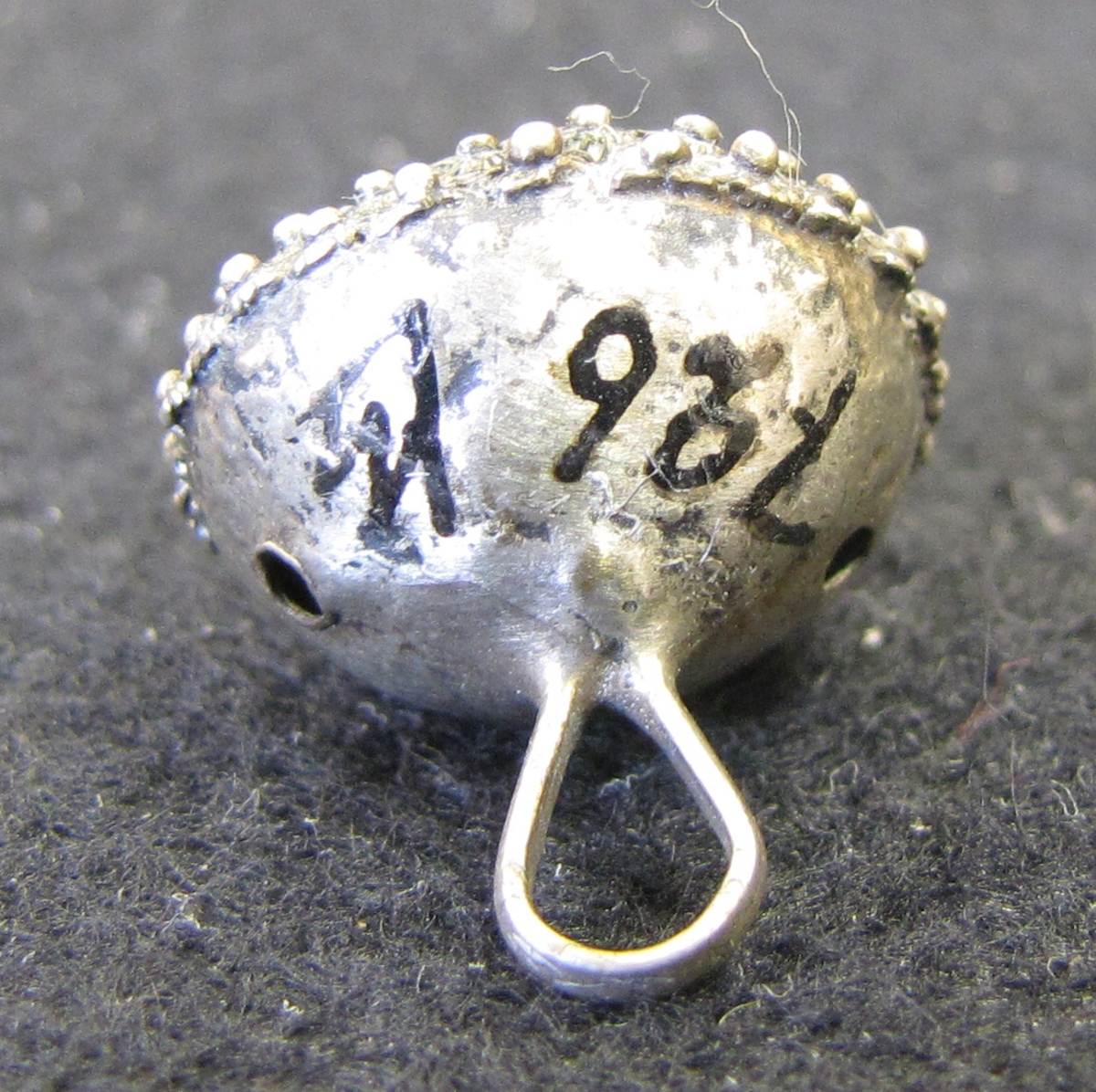 Silverknapp med riklig filigrandekor på ovansidan. Enligt museets katalog 1904-05 härrör knappen från Norge.