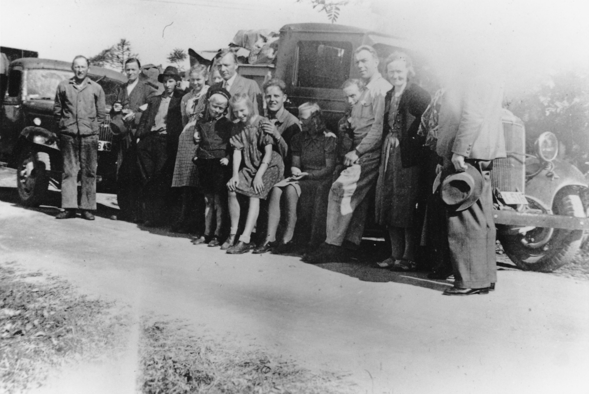 Prestefamilien Steinholt, med medhjelpere, fotografert foran lastebilene de brukte da de måtte evakuere Trondenes prestegård i 1942.
