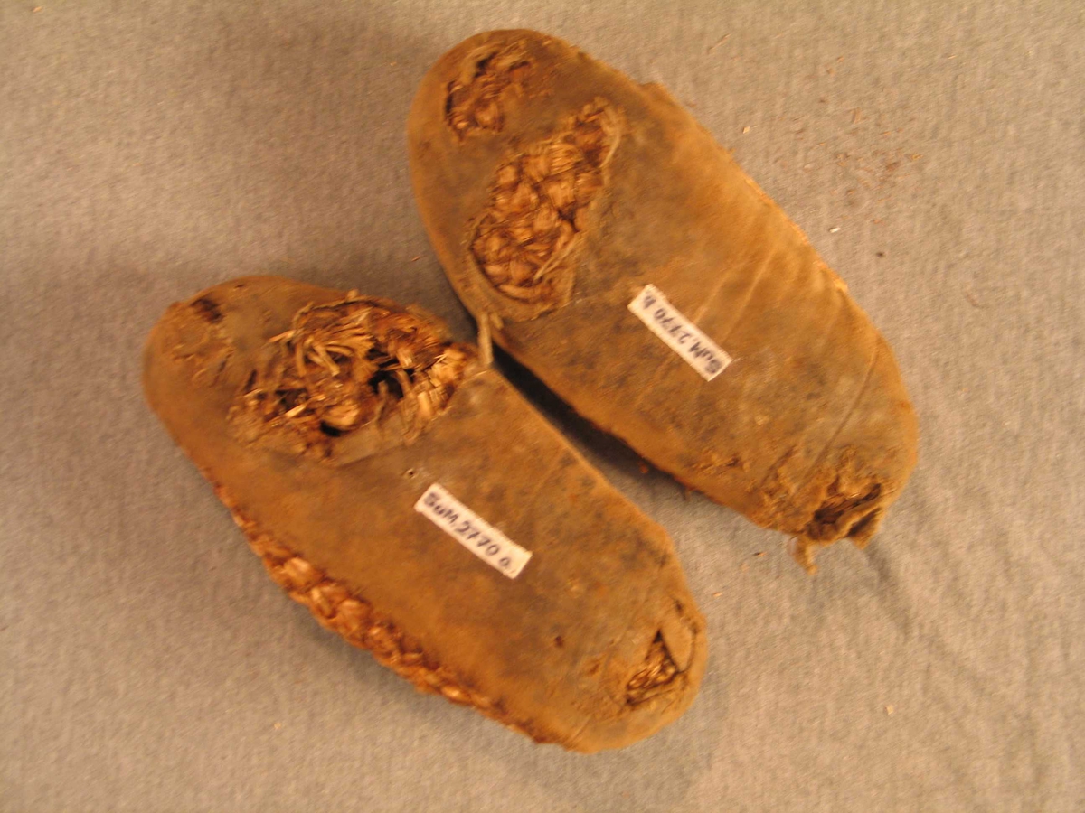 Fletta remser av halm som er sydde saman til sko. Påsydd trekk under av bomullsstoff