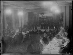 Gruppe menn og kvinner ved dekket langbord, festpyntet scene