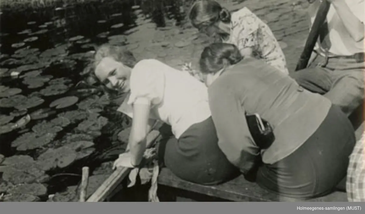 Tre unge kvinner og en mann plukker vannliljer fra en robåt. Se også ST.K.HE 2007-011-0127 til -0133.