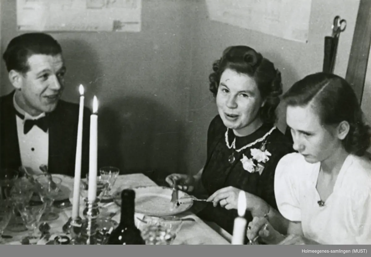To kvinner og en mann ved et middagsbord dekket til fest.