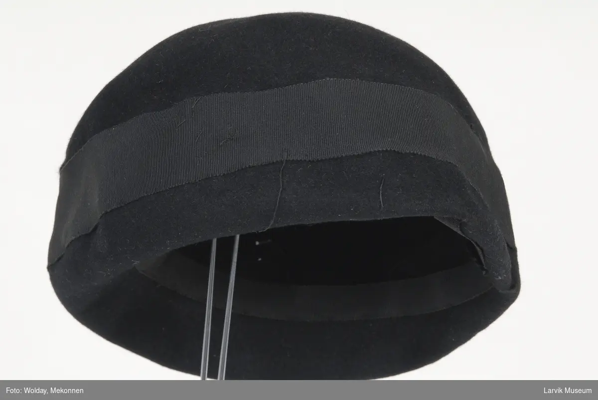 Form: sort filt, sort ripsbånd langs kanten og på
