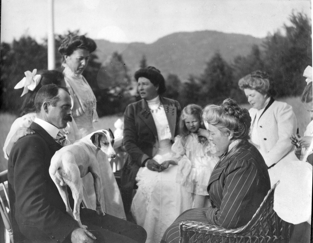 Verandaen på Østvang under Frøvik gård, 1910. Tommy, hunden "Sir", Baby Scott(gjemt), Aagot, Lalla, Bitte, Nanne og Elisa i samtale.