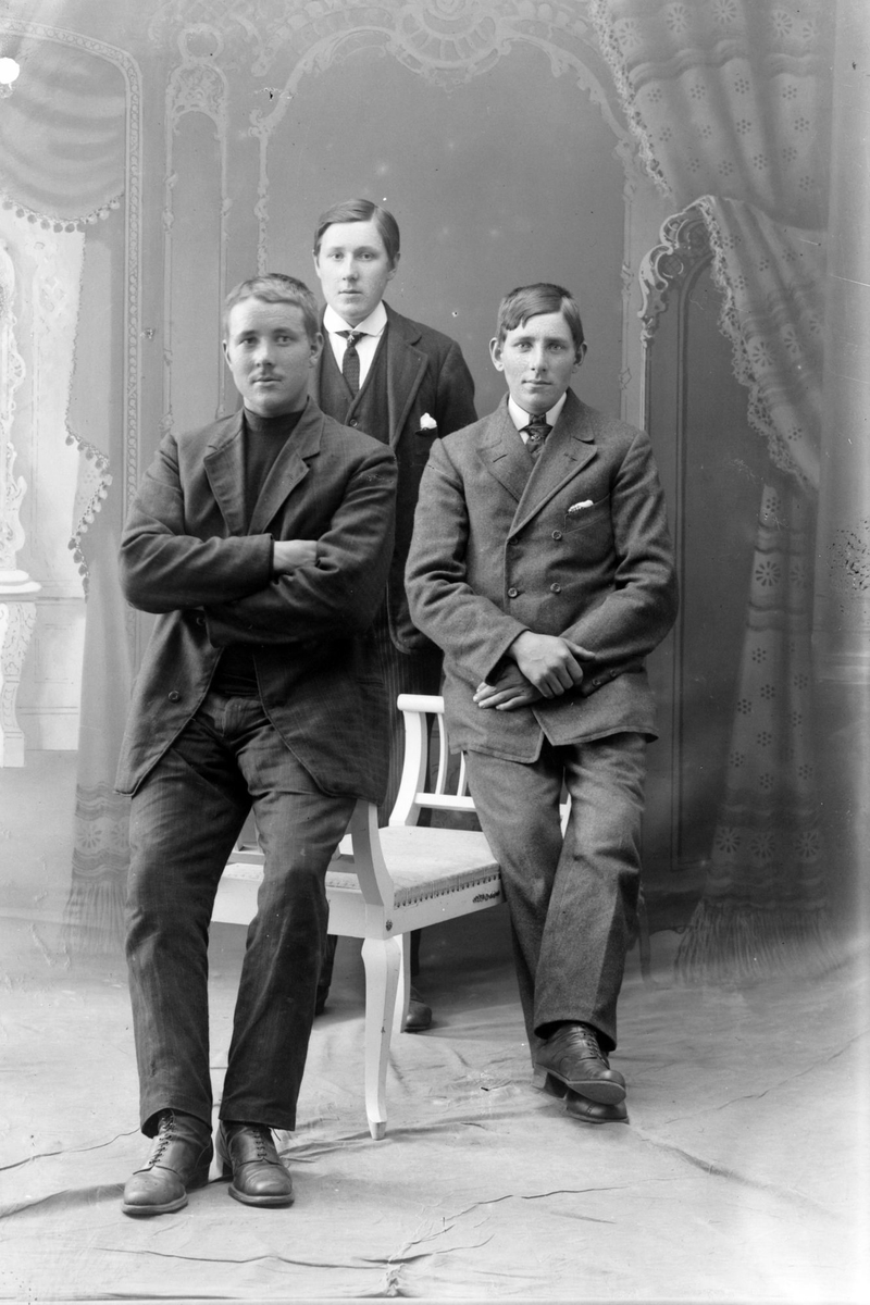 Studioportrett av tre menn ved en hvit benk.