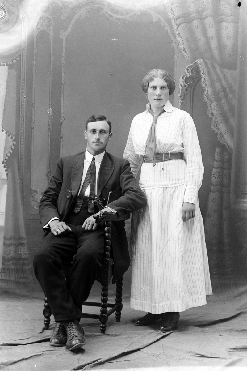 Studioportrett av en stående kvinne ved en mann som sitter.