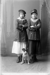 Studioportrett av to jenter med en hund foran seg.