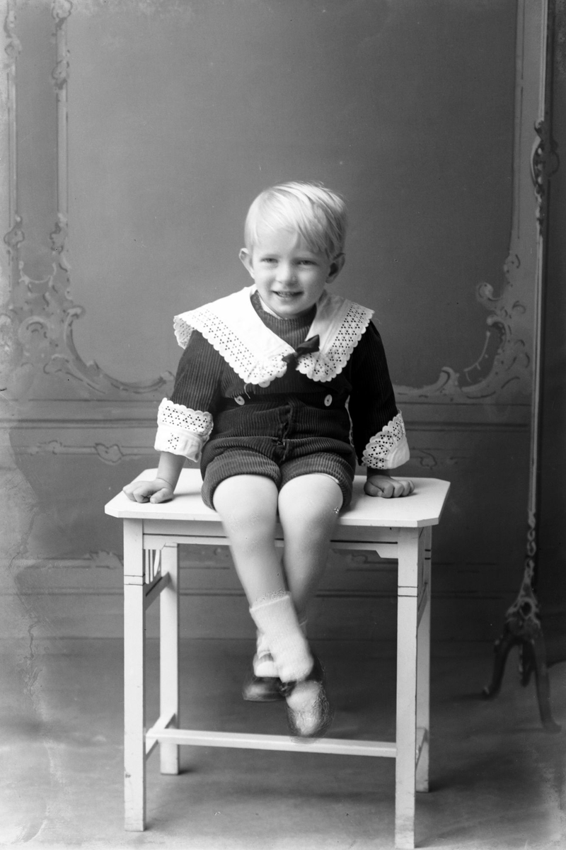 Studioportrett av en ung gutt sittende på et bord.