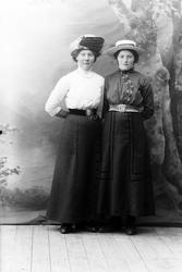 Studioportrett av to kvinner i helfigur.